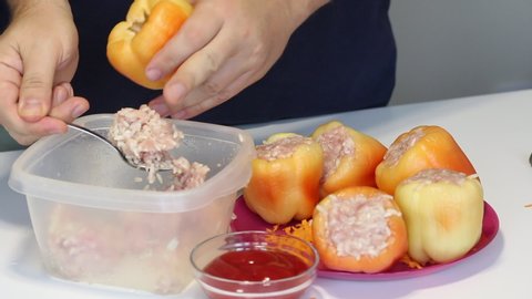A man prepares bell peppers stuffed with minced meat and rice. Pours minced meat and rice into pepper. She puts it on a plate