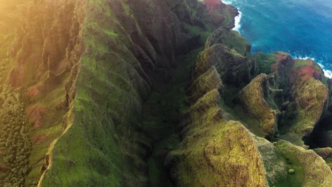 Cinematic nature at sunset. Golden sun light over the scenic landscapes on Hawaii tropical Island and Pacific ocean. Aerial 4K view on high mountain picturesque ridges rising over the blue waters
