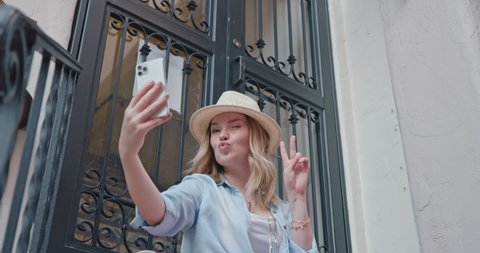 Attractive young woman is smiling when making selfie on smartphone. Beautiful stylish traveler is taking picture on her phone while relaxing during her sightseeing tour is the old Mediterranean city