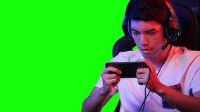 Esports gamer man playing game online on smartphone at home. Asian man controlling console with smart phone in video game. Young man leisure game in studio room and green screen at home.
