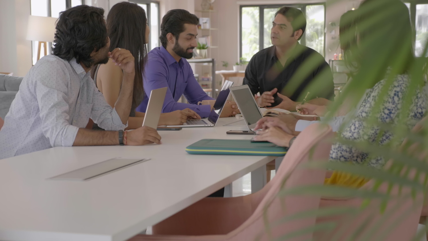 A group of corporate employees discussing using laptops in conference room at start up firm. A team of young male and female coworkers are talking interacting together in an modern office boardroom  Royalty-Free Stock Footage #1057760947