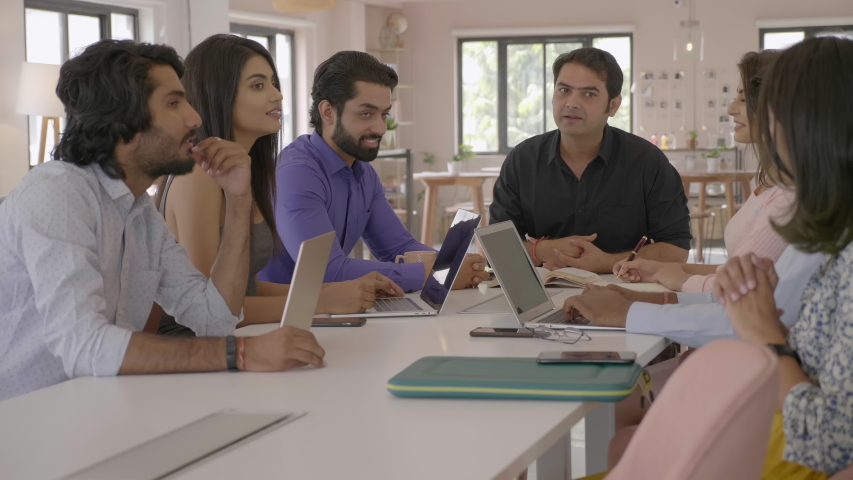 A group of corporate employees discussing using laptops in conference room at start up firm. A team of young male and female coworkers are talking interacting together in an modern office boardroom  | Shutterstock HD Video #1057760947