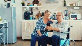Senior woman and disabled husband in wheelchair surfing on internet using smartphone in kitchen. Paralysied handicapped old elderly man using modern communication techonolgy. - Powered by Shutterstock - Get 15% off with code: PIKWIZARD15