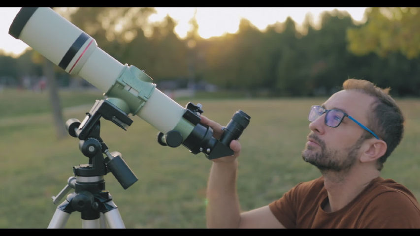 Astronomer with a telescope watching at the stars and Moon with blurred city background.	

