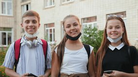 Portrait of pupils taking off protective medical masks from their faces and smiling against the background of the school building - Powered by Shutterstock - Get 15% off with code: PIKWIZARD15