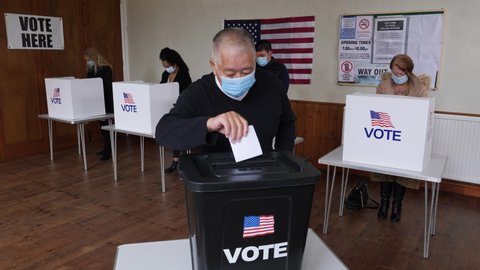 4K: Senior Male Chinese Voter voting at Polling Place for the USA Election. He wears a Face Mask while posting vote in the Ballot Box. Stock Video Clip Footage