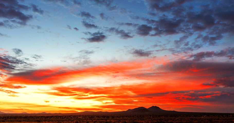 Crimson sunset spreads its fiery glow over the Mojave Desert mountain landscape with dynamic cloudscape - time lapse Royalty-Free Stock Footage #1057769869