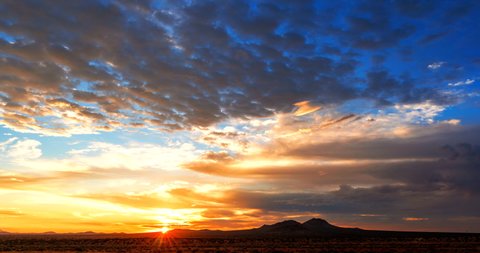 Crimson sunset spreads its fiery glow over the Mojave Desert mountain landscape with dynamic cloudscape - time lapse