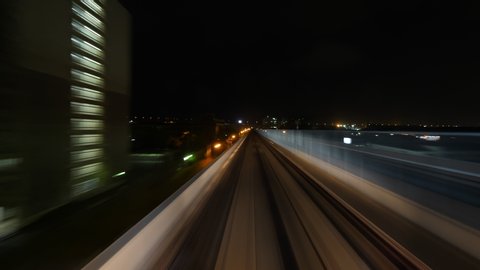 Front cabin view of modern driver-less metro train running through night Osaka city. Dark urban views and buildings sweep by, vehicle stop shortly at stations. Smooth time lapse shot