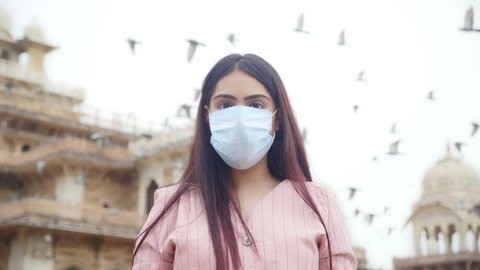 A young happy beautiful woman or female is standing outdoors removes face protective surgical mask and smiles looking at the camera or lens amid COVID 19 or Corona Virus epidemic or pandemic