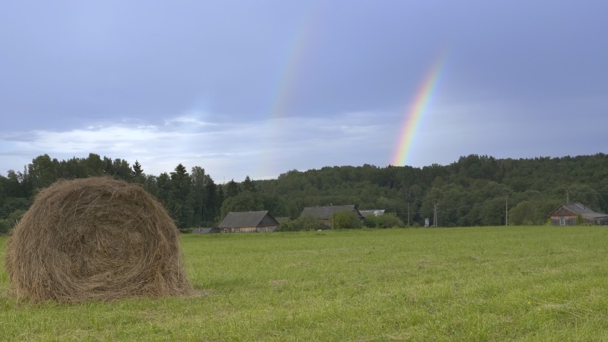 Shoot of double rainbow over green farm field. Rural landscape with hay bales on field and rainbow

