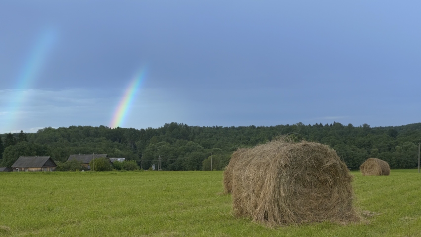 Shoot of double rainbow over green farm field. Rural landscape with hay bales on field and rainbow
