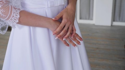 A girl stands in a white wedding dress. Close - up of hands