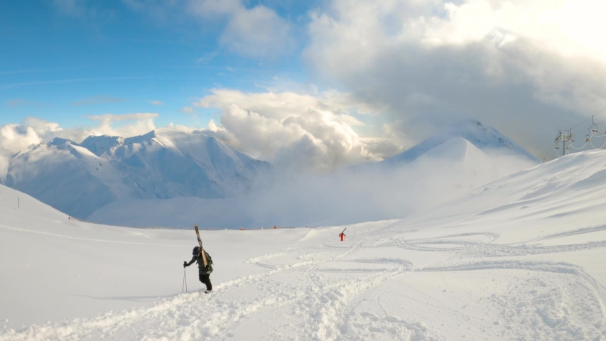 Two female freeride skiers hiking uphill and carrying his skis towards snowy mountaintop. Blue sunny day in spanish Pyrenees. Top view.