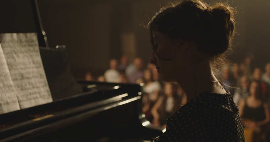4K Footage Of Female Pianist Plays In Beautiful Grand Piano On Stage In Concert . A woman plays the piano in the concert hall . Many unrecognizable , blurred people in the background .  Royalty-Free Stock Footage #1057777525