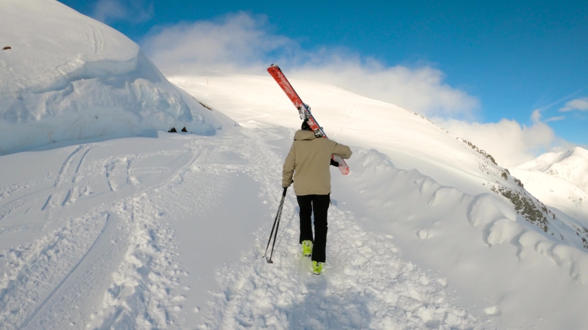 Freeride skier hiking uphill and carrying his skis towards snowy mountaintop. Blue sunny day in spanish Pyrenees. Back view.