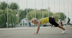 Sportswoman exercising on embankment in city. Side view of fit female athlete leaning on ground and lifting leg during fitness training on embankment.  4K RAW video record.