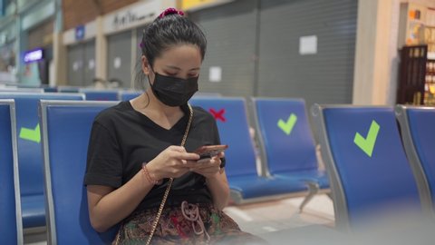 Asian woman wear black face mask sit down on a chair using smart phone, corona virus COVID-19 Pandemic, Social distancing sign public benches, new normal life, keep away distance 2 meters 6 feet away
