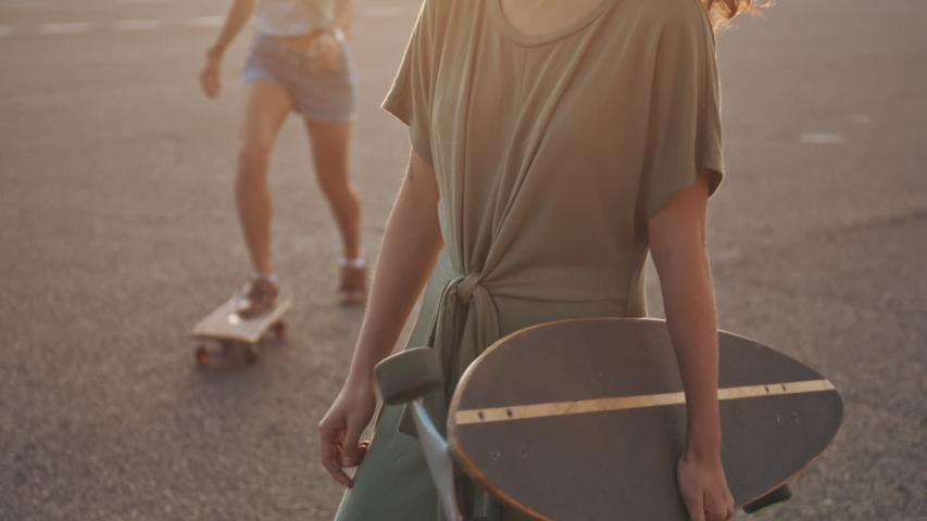 Outdoor portrait of two hipster friends with skateboard high five in sunshine city. Two fashion hipster women walking with coffee in hands at hot summer day and skateboarding lifestyle. Royalty-Free Stock Footage #1057779454