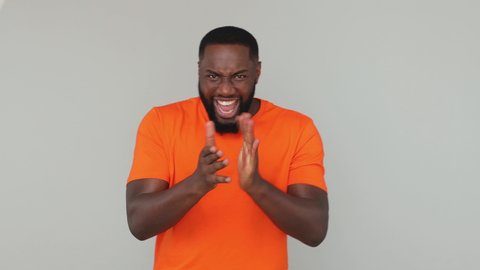 Young fun crazy african american guy 20s in orange basic t-shirt look at camera count countdown 1 2 3 one two three go celebrating doing win hands gesture isolated on grey color gray background studio