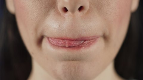 Can you resist the temptation? Cropped closeup of a beautiful full lipped woman licking her lips seductively.Slow motion 4K video. Blue background.