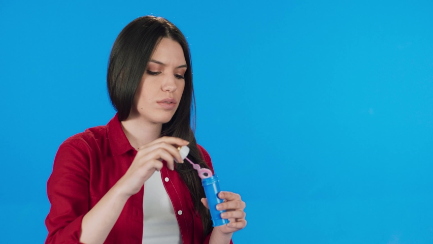The black-haired woman makes a bubble of soap bubbles on a blue background.