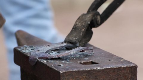 Close-up of a blacksmith's hammer bends a red-hot part. Pliers hold the horseshoe securely. The blacksmith demonstrates work.