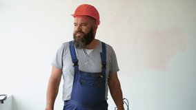 A bearded male construction worker is dressed in overalls and a protective helmet. maintains a video blog explaining