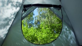 Travel concept. Point of view 4k video shoot of blue camping tent and blurry green summer forest as seen through entrance of tent.