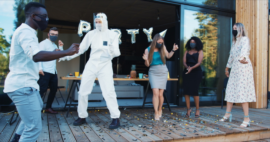 Epic COVID-19 party celebration. Happy diverse friends dance together with safety costumes and face masks slow motion.