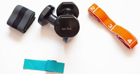 Athletics accessories. Dumbbells, resistance bands for working out at home. White background top view and copy space. Fitness equipment on stop motion video: film stockowy