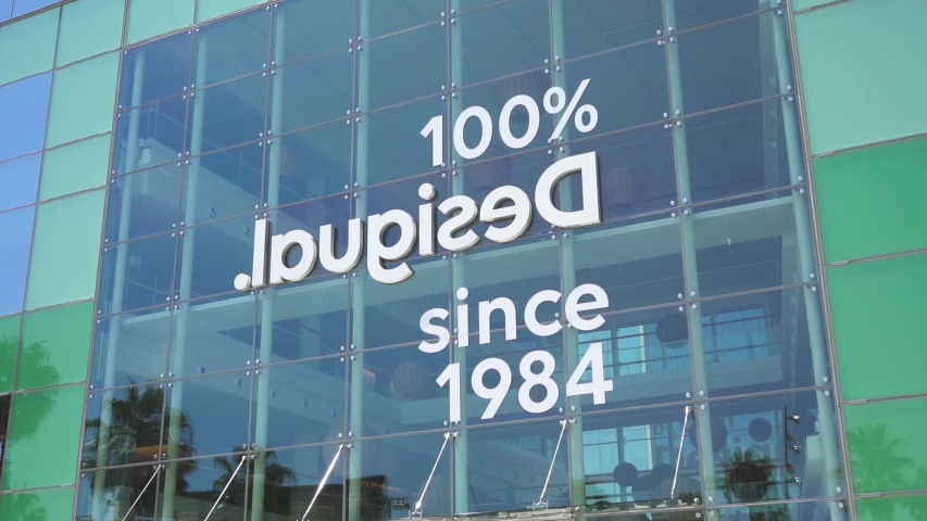 BARCELONA, SPAIN - AUGUST 09 2020 Desigual modern office building in Barceloneta. Detail of a banner in the facade with the text: 100% Desigual since 1984. Clothing brand headquartered in Barcelona. | Shutterstock HD Video #1057790656
