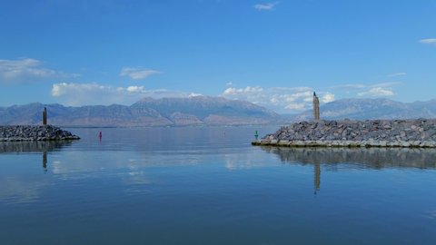Fly-through shot of the entrance to Saratoga Springs Marina on Utah Lake from the end of a red pontoon following channel buoys with distant mountains in the background reflecting off the calm water.
