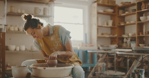 Young woman in pottery studio using pottery wheel, handmade ceramics, creative