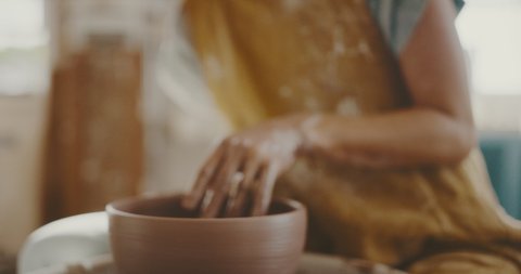 Woman potter in studio shapes clay bowl up close, handmade ceramics