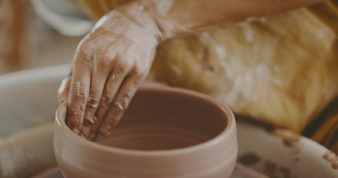 Woman potter in studio shapes clay bowl up close, handmade ceramics
