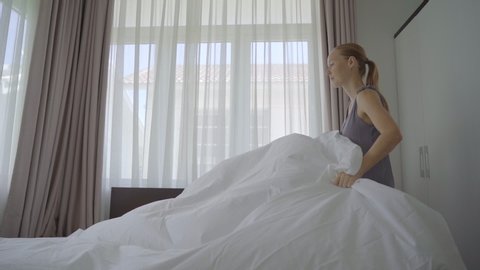 Slow-motion shot of a young woman changes bed linen in a room