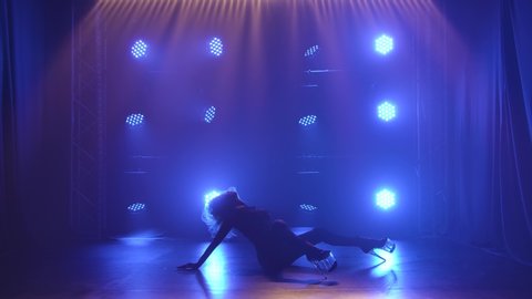 Sexy woman in stockings is dancing a Strip dance, strip of plastic. Silhouette of sensual blonde moving on a black background with blue spotlights. Slow motion.