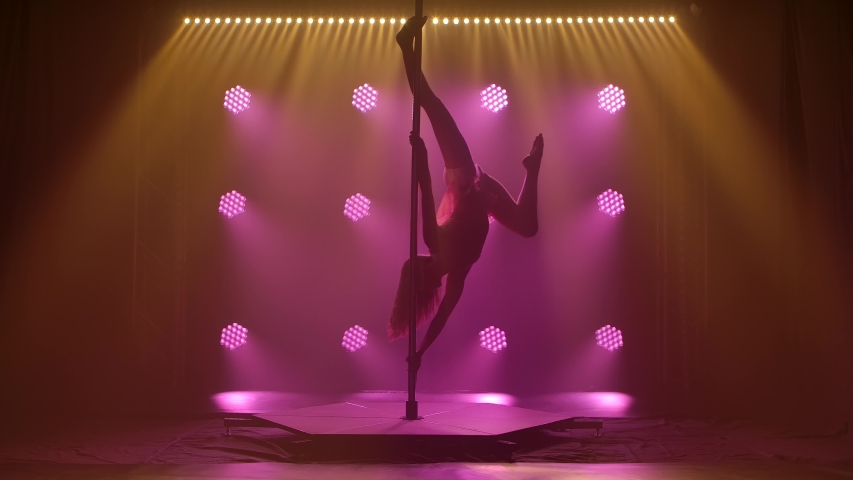 Beautiful pole atheletic performance by an athletic young female. Silhouette of an attractive body in a swimsuit on a smoky background. Slow motion.