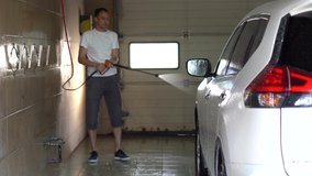 Man washing car with hose in driveway