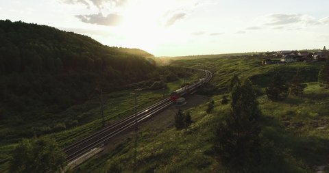 Passenger train by winding Trans Siberian railways near village in the Ural Mountains with beautiful sunset.  Aerial Photography, drone wide view at summer sunset