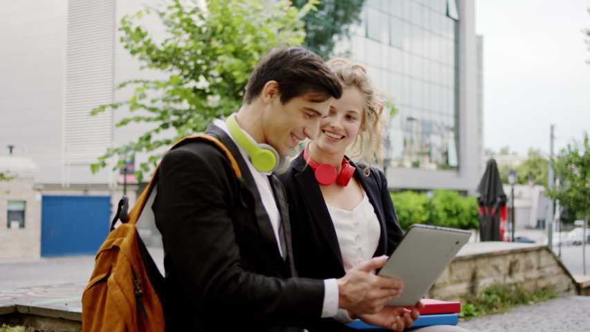 In the middle of the street with a big business building two office workers together take a sit using digital tablet to analyzing something beautiful curly hair lady and her attractive guy