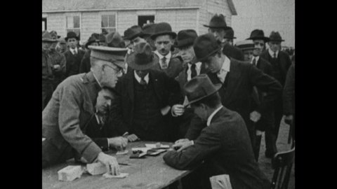 1910s: Men sit at table, take papers from other men. Man inspects other men's mouths. Men march in field.