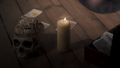 Scene of fortune-teller forecasting fate with tarot cards. Woman placing cards in order as mystic rite. Halloween divination in spooky esoteric atmosphere with candle and skull on background.