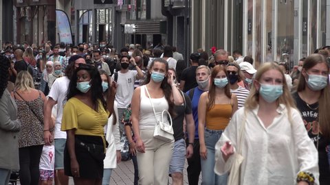 AMSTERDAM, NETHERLANDS – AUGUST 2020: Crowds of visitors walk through popular shopping street in Amsterdam, they are wearing compulsory face masks due to local Covid-19 corona virus regulation