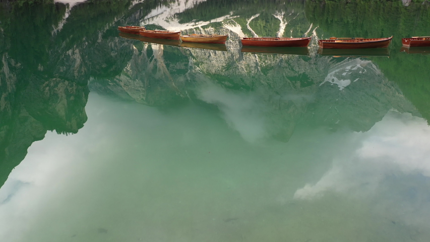 Drone flight over tranquil blue green waters and wooden rowing boats reveals beautiful mountain scenery at Pragser Wildsee (Lago di Braies ) in the Dolomites in Italy