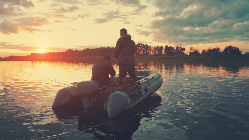 Friends fishing at sunset. Two amateur anglers fishing from the boat on a clam lake during sunset