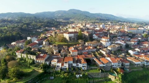 Aerial view of a beautiful little village in the city of Tui, located in Pontevedra province, Spain. Gable roof houses surrounded by trees and green hills.