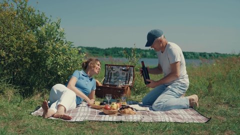 A couple, a man and a woman drink wine and talk cheerfully on a picnic on a Sunny summer day.