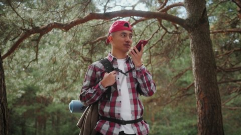 Asian Hipster Man sending voice messages with mobile phone at park, teenager student use audio message search on grass in park, korean backpacker walking tour, voice search
